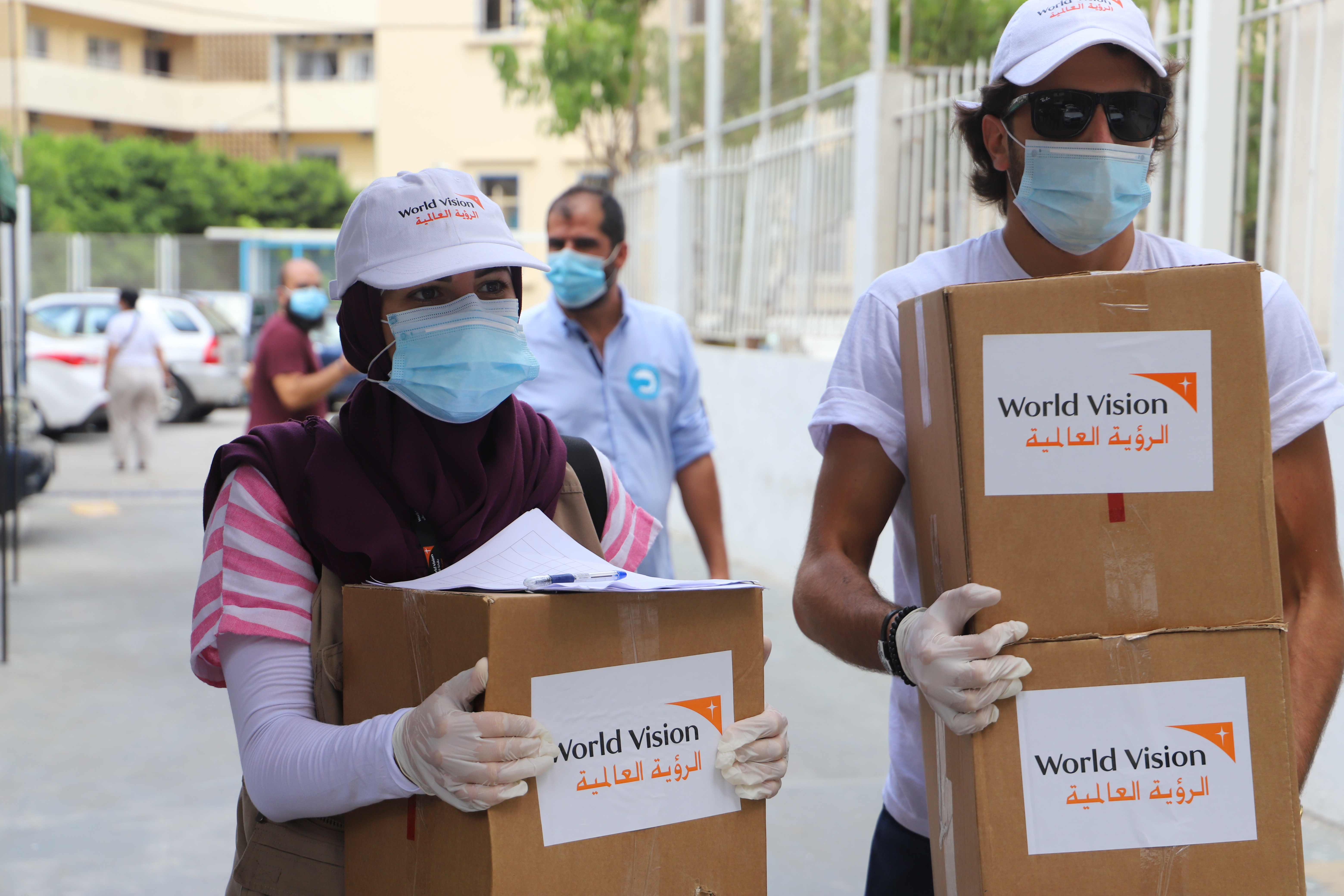 World Vision representatives wearing face masks, carrying boxes of emergency supplies
