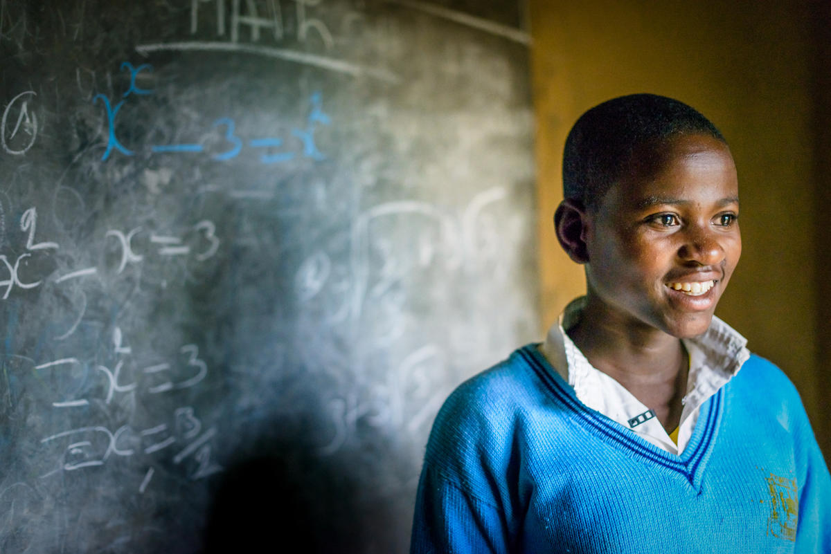 A 16 years old girl from Rwanda wears a blue school uniform writes maths work on the blackboard to prepare for an exam