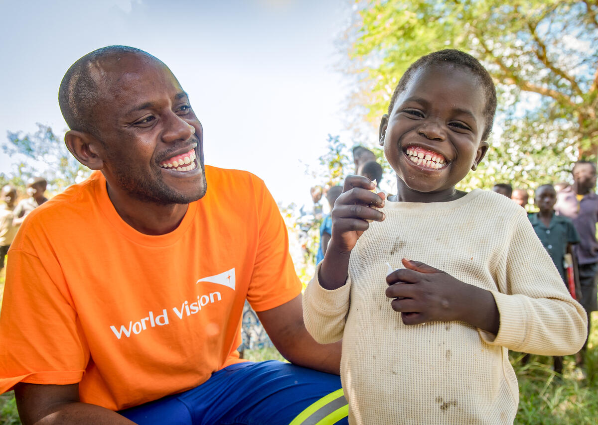World Vision staff, Matthew Sakala, helps 5-year-old Adam with a piece of birthday cake at the community wide birthday celebration hosted by World Vision