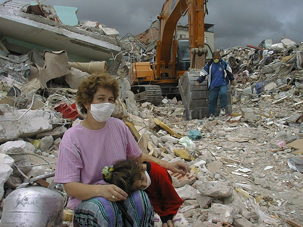 A woman wearing a facemask holds a little girl in her arms in fron ot a pile of rubble after the Turkey-Syria earthquake
