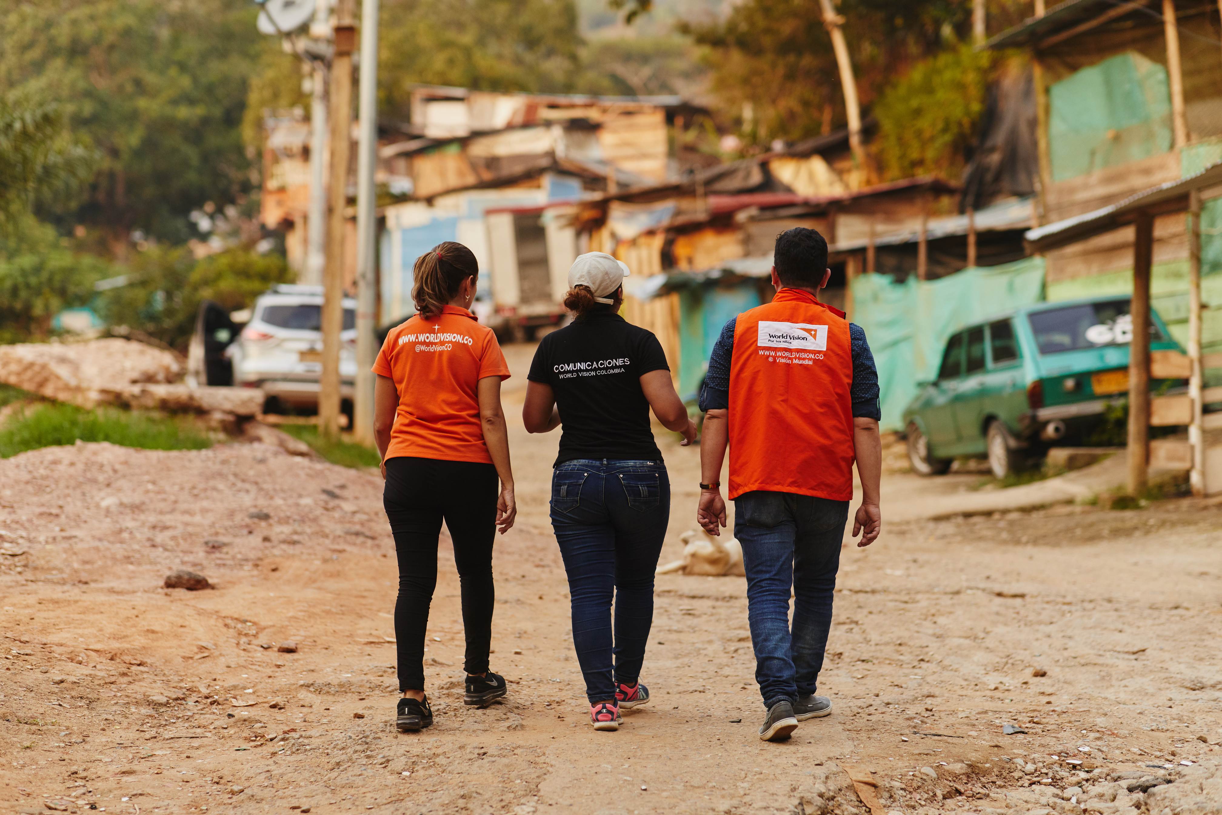 Two World Vision staff walk with a lady, backs to the camera, through streets in Colombia